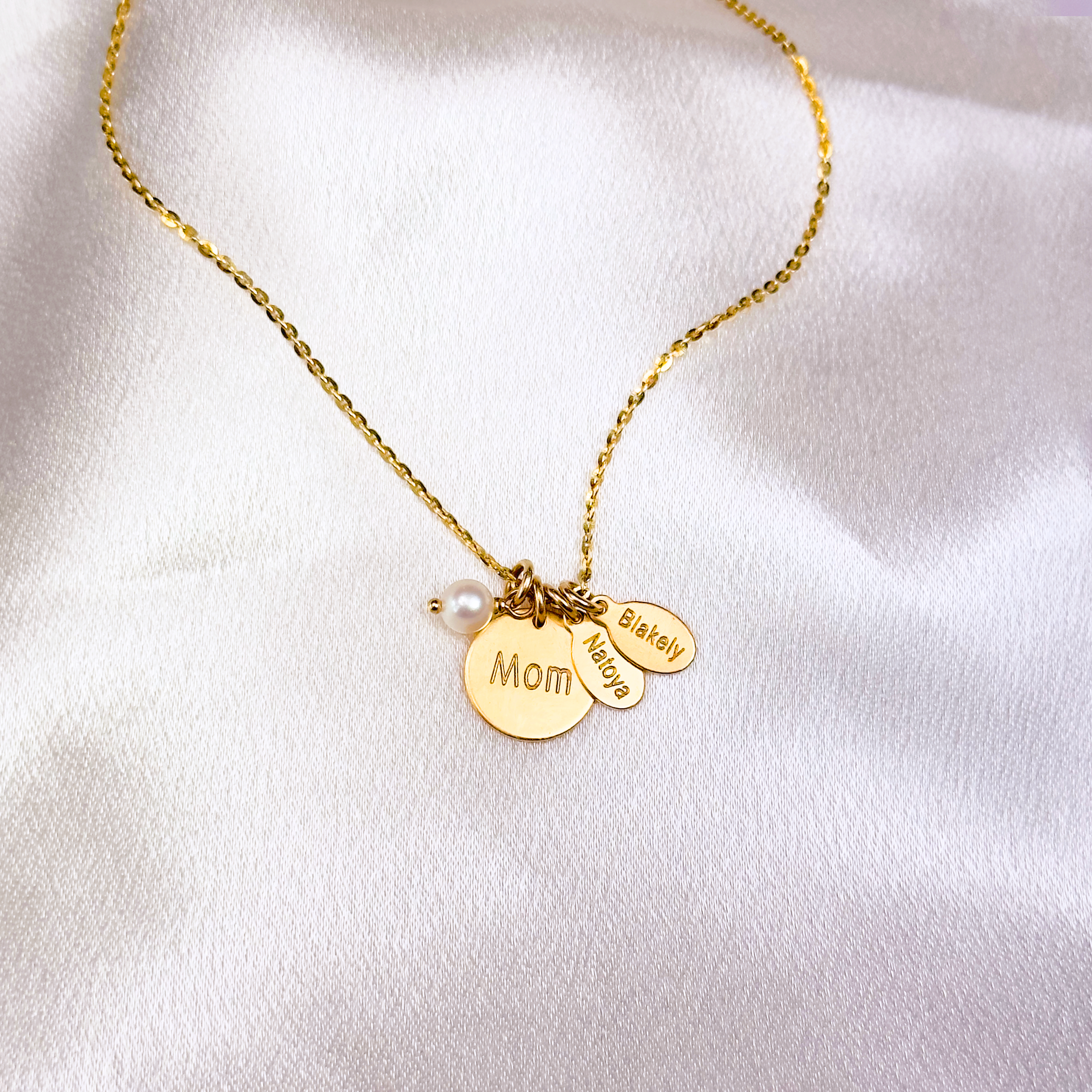 Gold disc and custom name tag necklace on white background. Elegant and timeless, personalized Mother's necklace features a round disc with your name, oval tags for your kids and a freshwater pearl charm. Mom necklace, kids names, pearl charm.