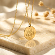 Close-up of a gold monogram disc necklace on soft fabric, featuring engraved initials on a round pendant with delicate chain.