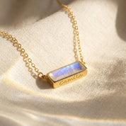 Close-up of a natural moonstone bar necklace on soft fabric, showing the horizontal June birthstone pendant in a gold setting.