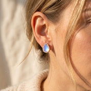 Model wearing natural rainbow moonstone stud earrings, showing the delicate teardrop size and soft iridescent glow for everyday gemstone jewelry.