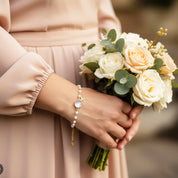 Bride wearing personalized initial and birthstone bracelet, June pearl and August peridot charms, elegant bridesmaid jewelry gift idea for wedding day, custom gold charm bracelet with initial letter and gemstone.