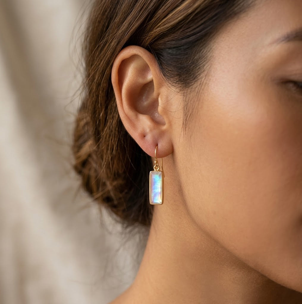 Natural moonstone bar earrings worn on a model, showing rectangular June birthstone drop earrings in a gold setting.