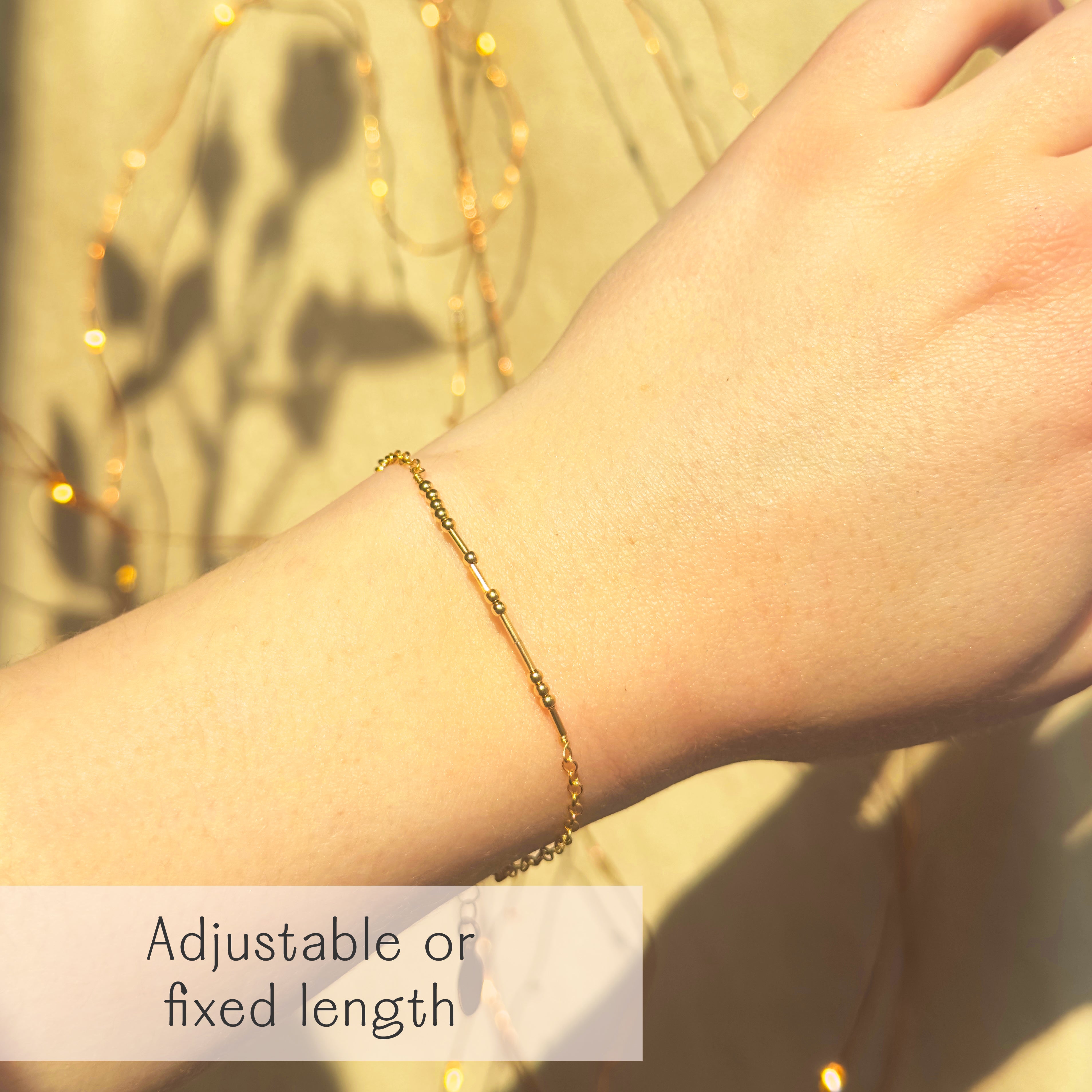 Gold Morse code bracelet worn on wrist with adjustable clasp, featuring delicate beadwork that hides a secret message. A dainty bracelet gift for girlfriend, boyfriend, best friend, or sister. Perfect for birthdays, anniversaries, Christmas, Valentine’s Day, or long distance relationships. Handcrafted in gold filled, sterling silver, and rose gold filled options.