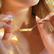 Gold Morse code bar necklace being held at the collarbone, skinny horizontal plate engraved with secret message dots and dashes on a delicate 14K gold filled chain, minimalist personalized jewelry, custom hidden message necklace for her, meaningful gift idea for best friend, daughter or girlfriend.