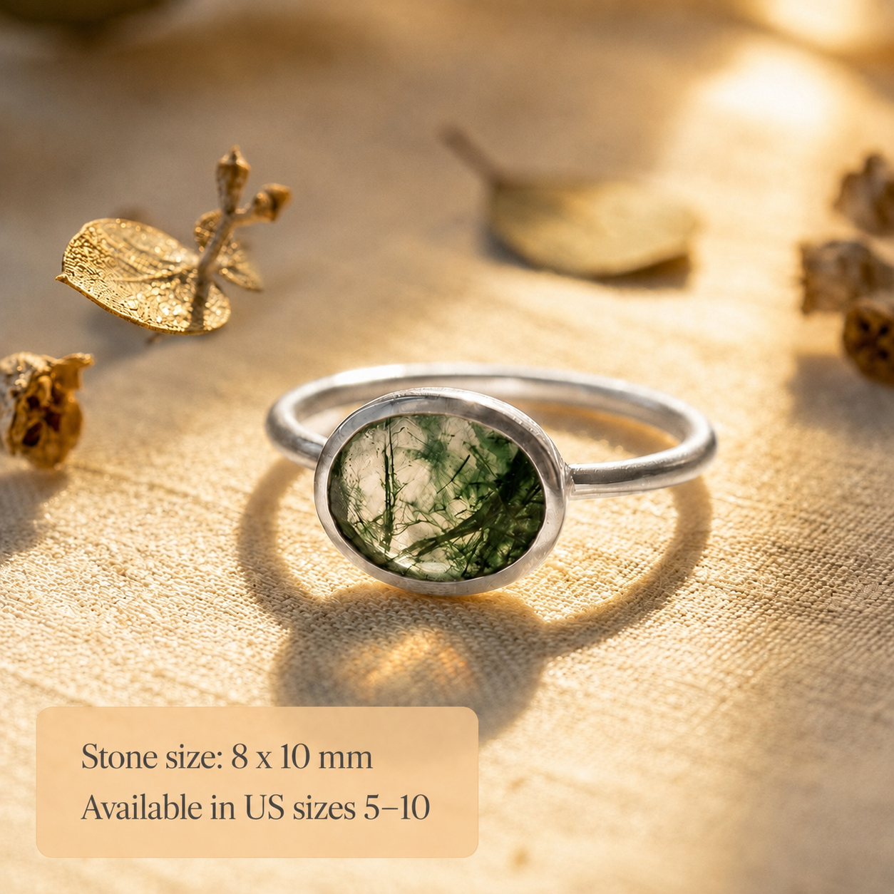 Sterling silver moss agate ring with oval 8x10mm green gemstone shown on warm textured background with soft shadow.
