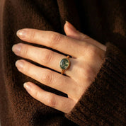 Moss agate ring worn on hand with a dark sweater, showing the oval green stone size and natural everyday styling.