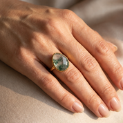 Large faceted moss agate ring worn on woman's hand showing natural green inclusions and polished gold bezel setting