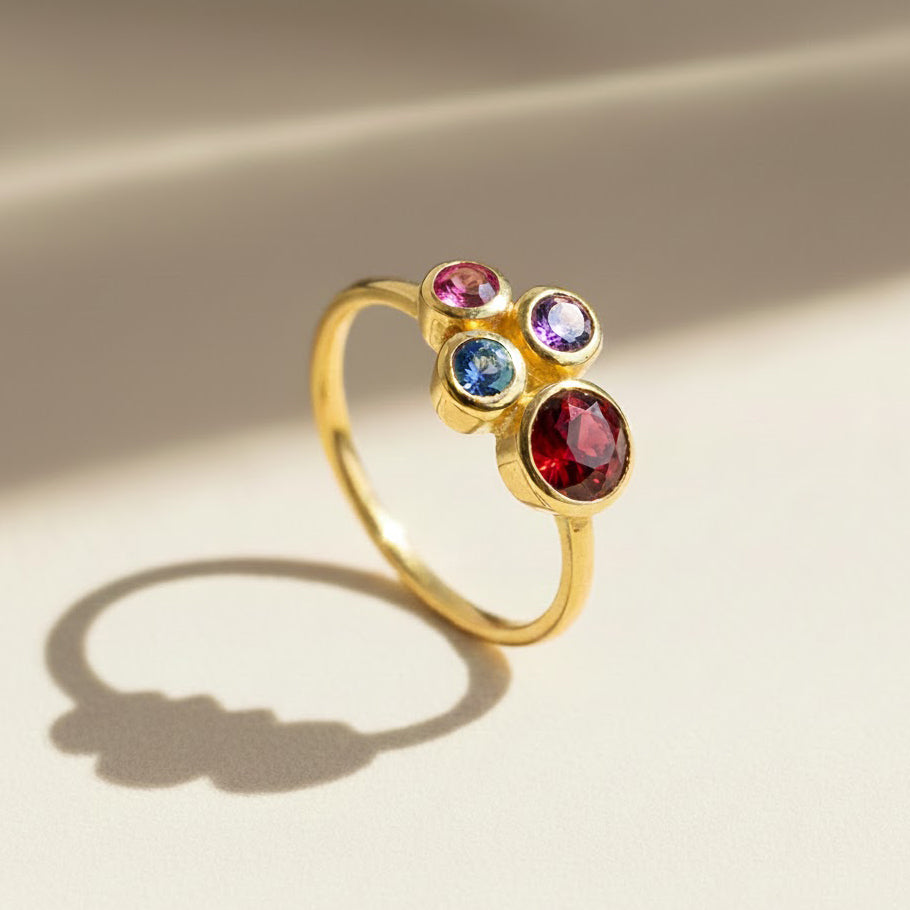 Single gold plated custom mother of three birthstone ring. Mom stone is January Garnet, kid's stones are October pink tourmaline, September  sapphire and February Purple Amethsyt.