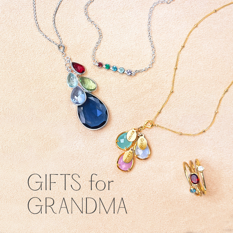 A pink background with a teardrop cascade grandmother necklace, a horizontal birthstone bar necklace, a custom engraved name and birthstone danique necklace, and a personalized mother's ring set, oval gemstone and tiny round ring set, gifts for grandma.