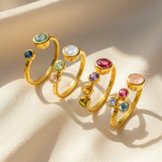 Gold personalized birthstone ring for mom of three, featuring a bold 5mm center stone representing the mother surrounded by three dainty 3mm child stones, all bezel-set for durability. Styled in a warm gold finish and photographed on satin, this adjustable ring is a thoughtful Mother’s Day or Christmas gift. A timeless handcrafted piece for moms wanting meaningful, sentimental family jewelry celebrating their children.