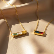 Personalized birthstone bar necklaces in gold with rectangular gemstones on soft fabric.