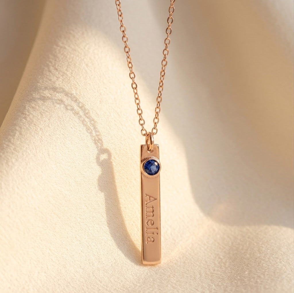 Single engraved name bar necklace with blue birthstone charm shown on model