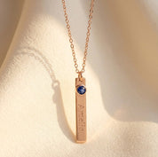Single engraved name bar necklace with blue birthstone charm shown on model