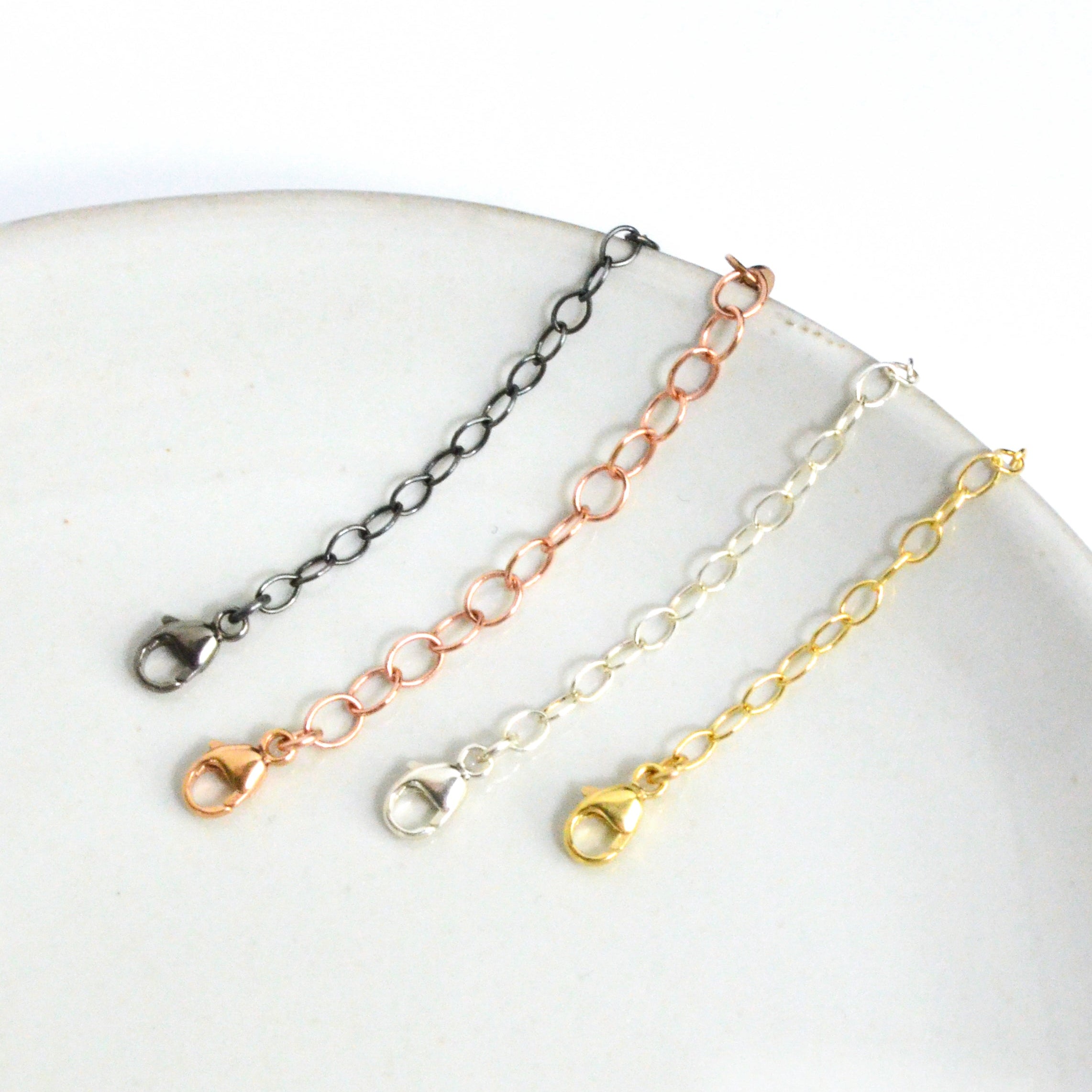 Necklace extender chains in sterling silver, gold filled, rose gold, and oxidized blackened silver displayed on a white plate. Adjustable chain extender adds 1–6 inches to necklaces or bracelets, making it perfect for layering jewelry or customizing fit. Popular jewelry accessory gift for women who love delicate, minimalist necklaces.
