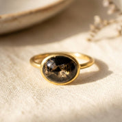 Oval black obsidian cabochon ring in gold setting on beige fabric with soft natural light