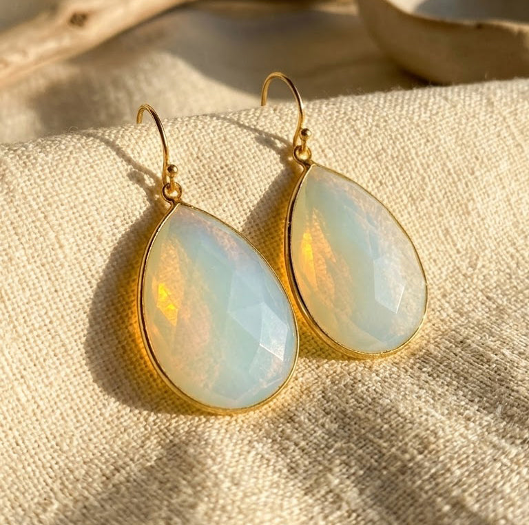 Opalite teardrop earrings in yellow gold vermeil displayed on cream fabric in warm natural sunlight.