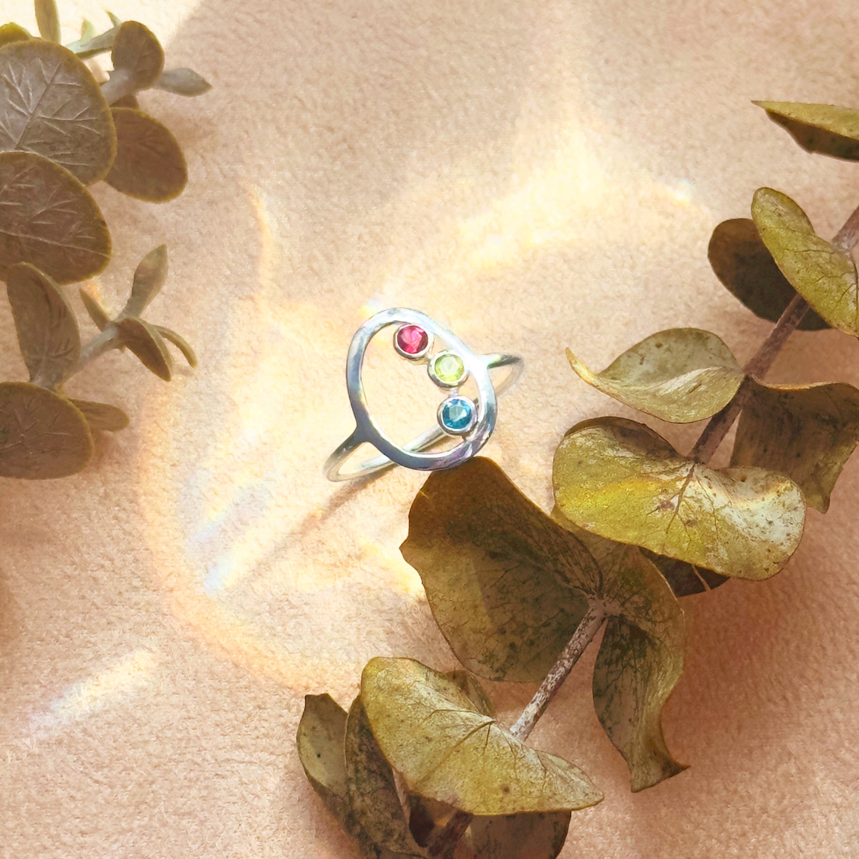 gold bezel custom mothers birthstone ring on silk fabric, minimalist family gemstone ring january garnet february amethyst march aquamarine