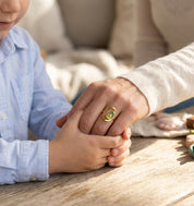 Gold mother and child birthstone ring worn on moms hand in warm natural light.