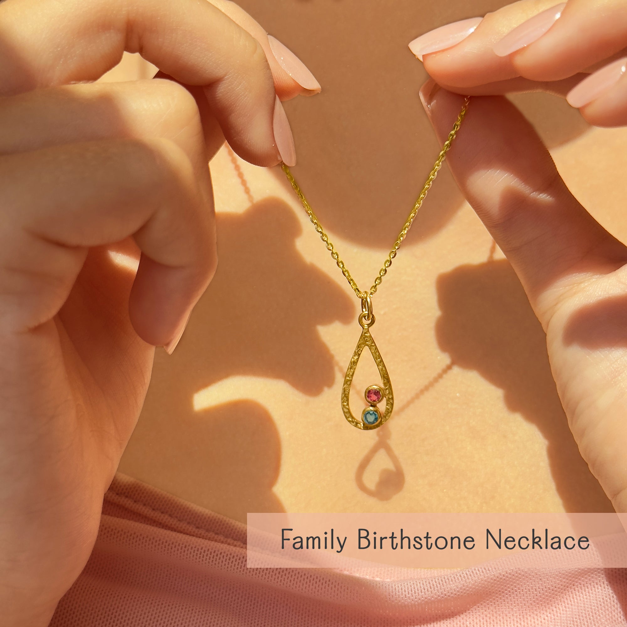 Hands holding personalized birthstone necklace for mom with colorful family birthstones in teardrop pendant