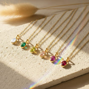 Oval cut birthstone bezel pendant necklaces displayed on textured neutral stone, featuring multiple gemstone colors representing different birth months. Dainty gold birthstone necklaces arranged in a row, highlighting minimalist bezel set design and delicate chain. Personalized birthstone jewelry perfect as a custom gift for her, Valentine’s Day gift, mom necklace, or meaningful everyday gemstone pendant.
