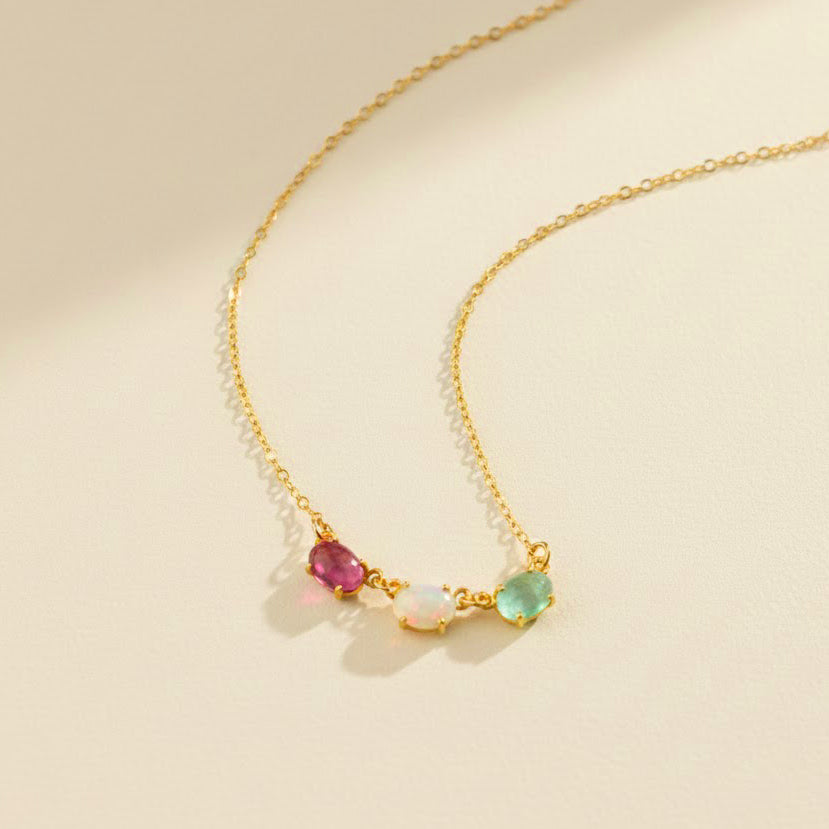Elegant horizontal oval birthstone necklace displayed on ivory background, featuring bezel-set oval gemstones including peridot, emerald quartz, moonstone, and blue topaz. A custom multi-stone mother necklace ideal for engraving a child’s name or birthdate on the back for sentimental meaning. Perfect Christmas or Mother’s Day gift for moms, grandmas, or new mothers who want personalized family jewelry made in high-quality gold, rose gold, or silver.