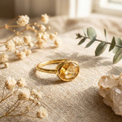 Oval citrine ring styled on soft neutral fabric with dried florals, featuring a bezel-set yellow citrine gemstone in a delicate gold band. Minimalist birthstone ring with an elegant, organic aesthetic, designed for stacking or solo wear. Ideal as a November birthstone gift, dainty gemstone ring for women, and meaningful jewelry for moms, daughters, or partners. Perfect for birthdays, anniversaries, Mother’s Day, and timeless everyday style.