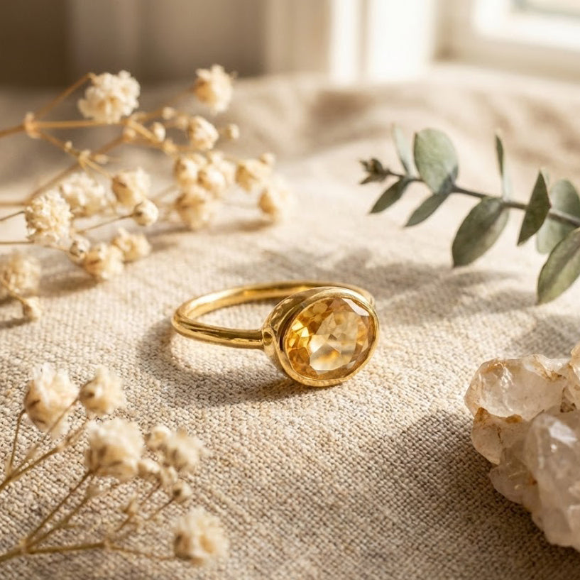 Oval citrine ring styled on soft neutral fabric with dried florals, featuring a bezel-set yellow citrine gemstone in a delicate gold band. Minimalist birthstone ring with an elegant, organic aesthetic, designed for stacking or solo wear. Ideal as a November birthstone gift, dainty gemstone ring for women, and meaningful jewelry for moms, daughters, or partners. Perfect for birthdays, anniversaries, Mother’s Day, and timeless everyday style.