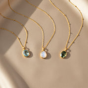 Dainty oval gemstone necklaces displayed on a soft beige background in warm sunlight, featuring three bezel-set stones in blue, iridescent moonstone white and deep green on delicate gold satellite chains. Minimalist birthstone or gemstone pendant necklaces perfect for everyday wear or layering, a meaningful gift for her, mom, sister or best friend for birthdays, Mother’s Day, Christmas, anniversaries or bridesmaid jewelry.