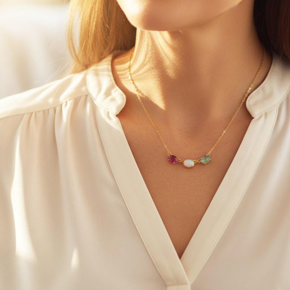 Woman wearing horizontal oval birthstone necklace with custom family gemstones in a minimalist bar layout, perfect for moms wanting child name engraved jewelry. Shown with emerald quartz, peridot, and blue topaz birthstones. A meaningful Christmas gift for mom or grandma, this personalized multi-stone necklace symbolizes each child and creates a heartfelt piece of family jewelry crafted in gold, rose gold, or sterling silver.