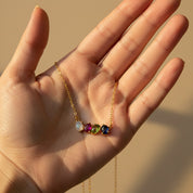 Hand holding custom oval cabochon birthstone necklace with multiple gemstones symbolizing children or loved ones. Personalized family necklace designed as a meaningful mom gift, grandma gift, or sentimental birthstone jewelry.