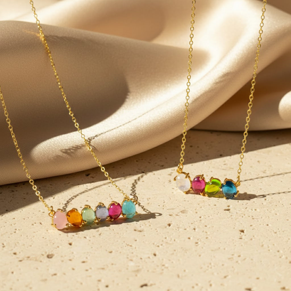 Oval cabochon birthstone necklace displayed on soft neutral fabric, featuring colorful gemstones set in gold. Minimalist personalized birthstone jewelry designed as a family necklace or meaningful gift for mom.