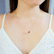 Model in white top is wearing a gold filled oval prong set cabochon necklace with pink chalcedony, moonstone and purple amethyst birthstones. 