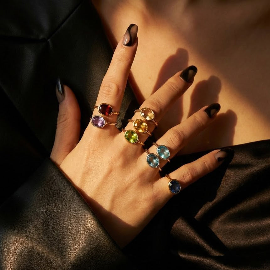 Hand wearing stacked gemstone rings including oval clear quartz ring in gold, modern mix and match ring styling