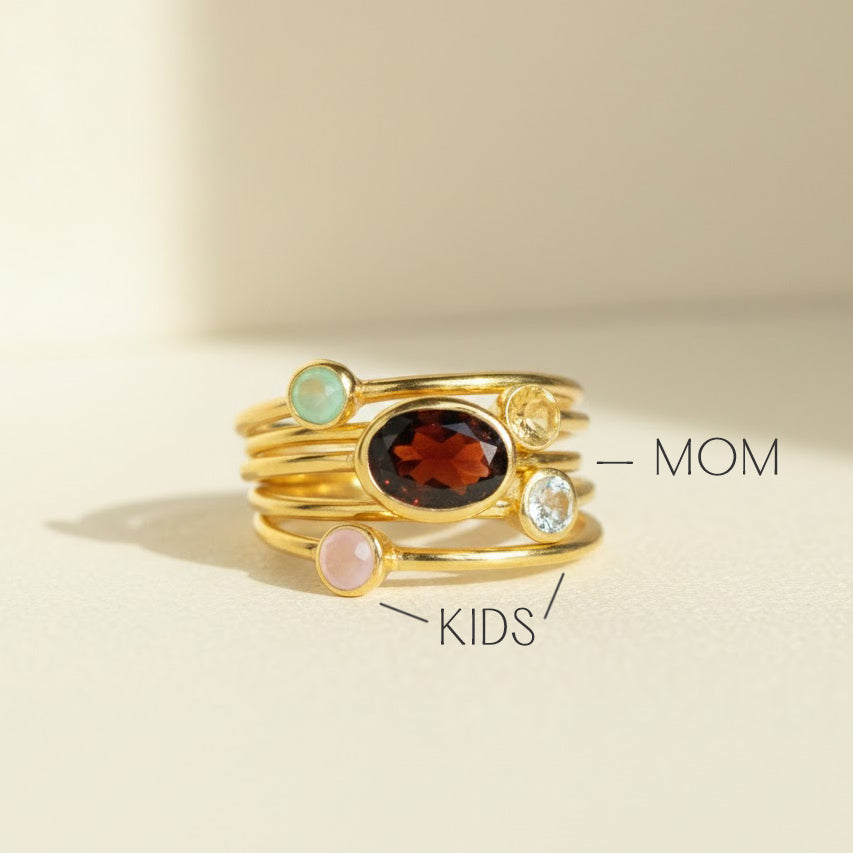 Explainer image showing what the stones mean in this custom mothers ring set: large oval birthstone represents MOM and tiny round birthstones represent KIDS, personalized family birthstone ring set in gold vermeil, dainty minimalist stacking ring combo designed as a meaningful keepsake gift, customize birth months such as February amethyst, April diamond/clear stone, and August peridot, perfect for Mother’s Day, new mom, and grandma jewelry