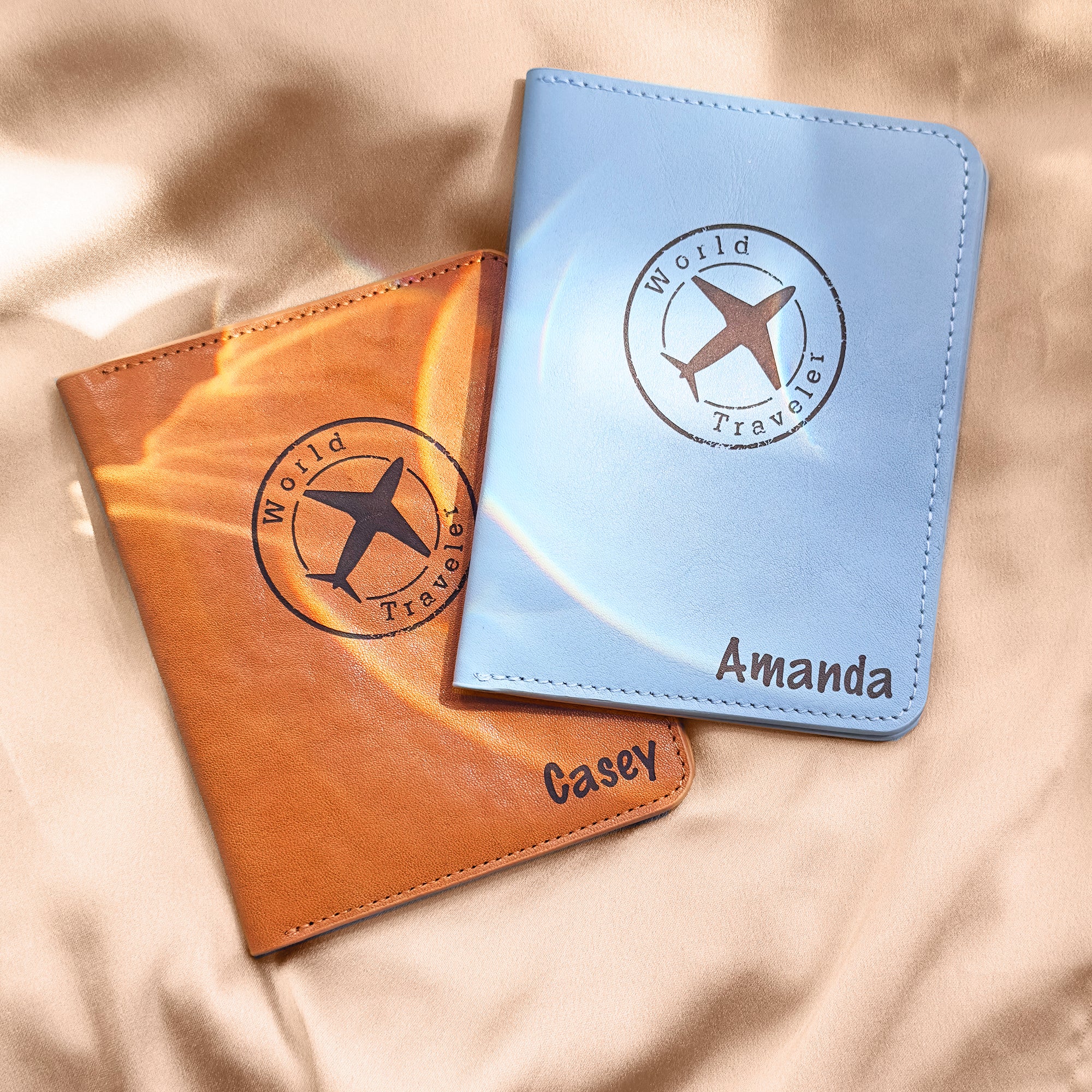 Two personalized leather passport covers with airplane “World Traveler” design, custom engraved with the names Casey and Amanda. One holder is classic brown and the other is light blue, both crafted from high-quality faux or genuine leather. These custom travel wallets are ideal for couples, best friends, or honeymoon gifts. A thoughtful travel accessory for her or him, perfect for destination weddings, anniversary trips, or globe-trotting adventures. Makes a unique and useful personalized travel gift.
