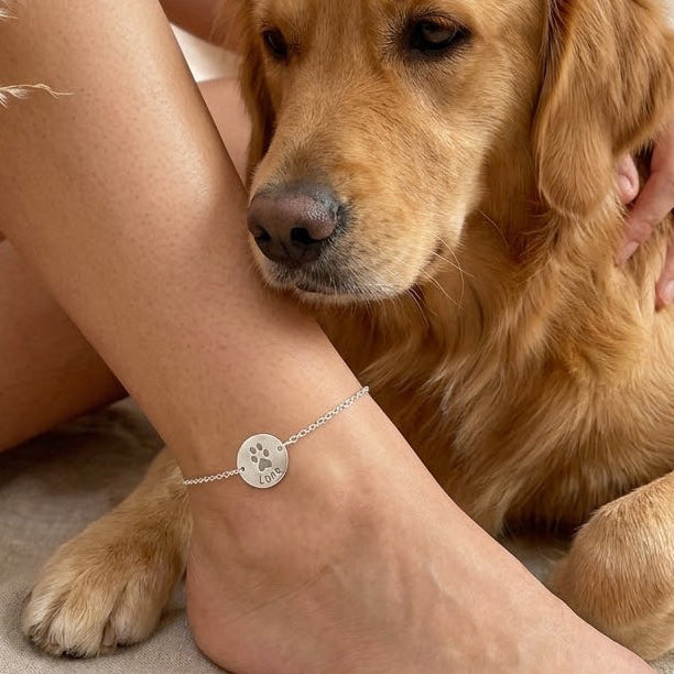 Personalized paw print anklet with engraved pet name in sterling silver worn beside golden retriever