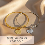 Custom paw print bangle bracelet hanging with soft lights, showcasing engraved pet name and paw print on a polished disc charm. Designed for dog moms, cat moms, and pet lovers who want sentimental personalized jewelry. Adjustable wire bangle fits comfortably for daily wear. Available in sterling silver, yellow gold, or rose gold. Ideal for gifting as pet memorial jewelry, birthday gift, Christmas gift, or meaningful keepsake for women.