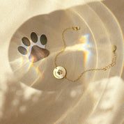 Gold personalized paw print anklet with round engraved pet disc displayed beside paw print keepsake