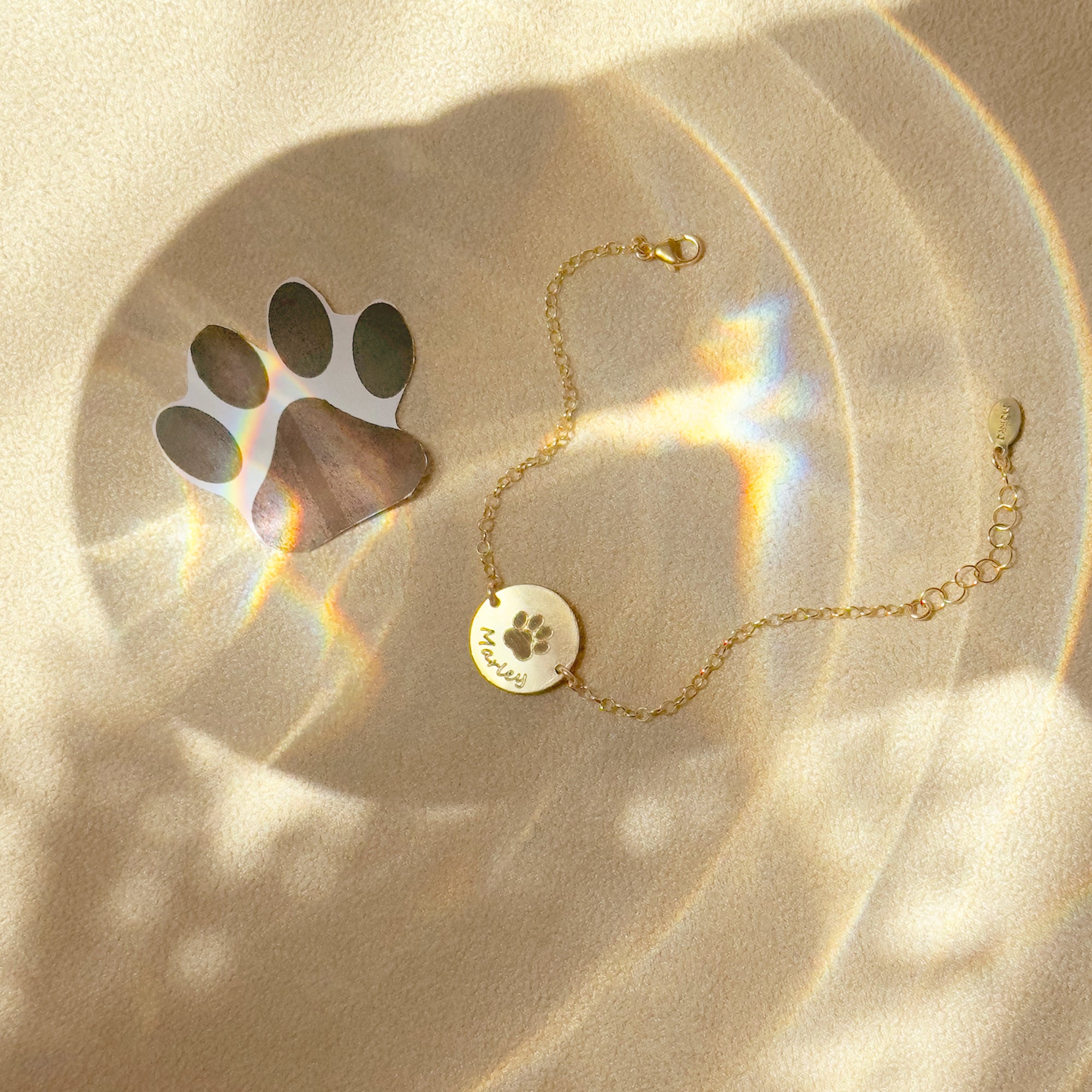 Gold personalized paw print anklet with round engraved pet disc displayed beside paw print keepsake