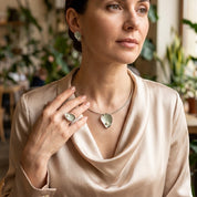 Woman wearing matching sage green sculptural necklace earrings and adjustable ring with pearl accents