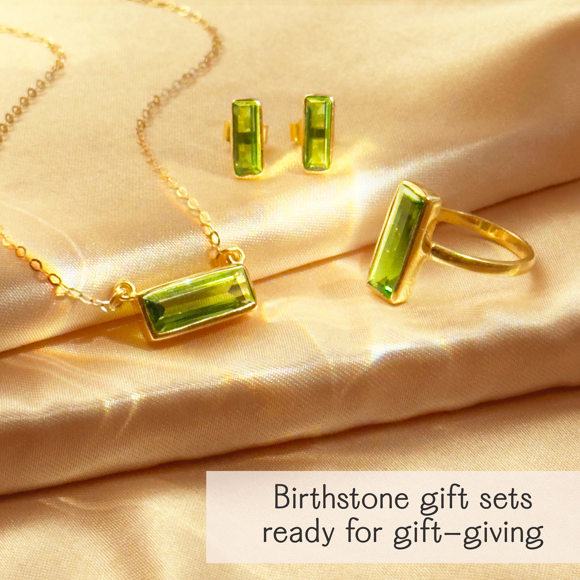 Green peridot baguette jewelry set—bar necklace, stud earrings, and statement ring in 14k gold filled with hydro gemstones—shown on champagne satin with “Birthstone gift sets ready for gift-giving.” August birthstone set; perfect birthday or bridesmaid gift.