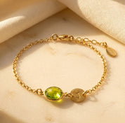 Personalized gold peridot initial bracelet with round faceted August birthstone and engraved disc charm.