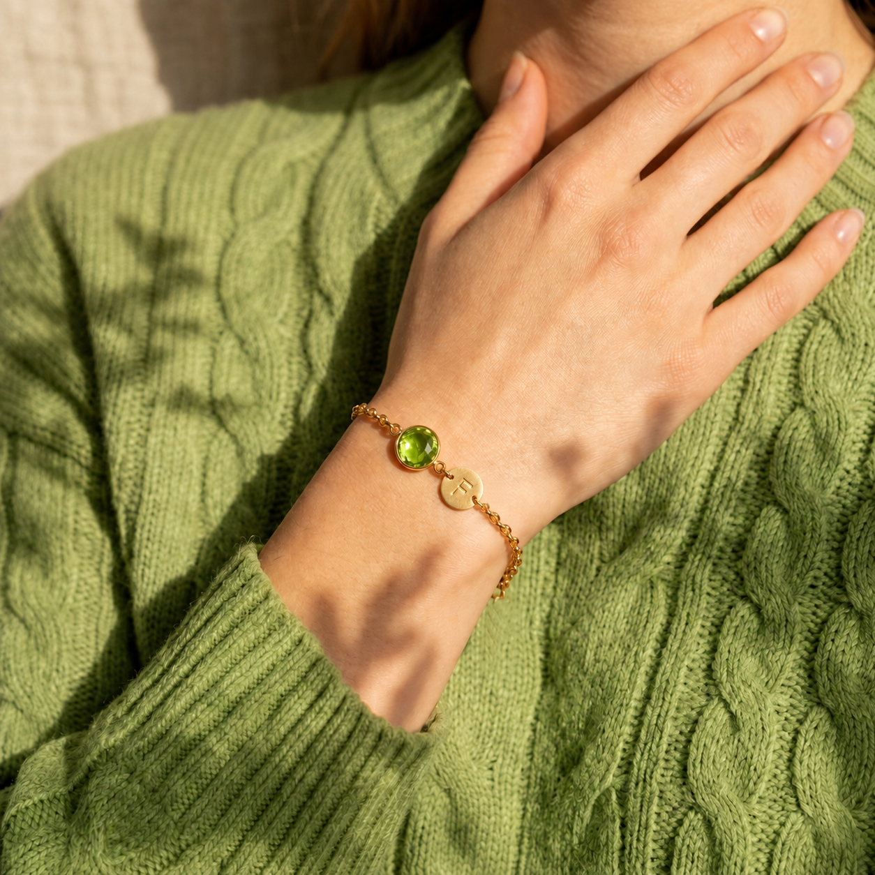 Woman wearing a gold peridot birthstone bracelet with personalized initial charm and green sweater.