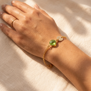 Close-up of a gold peridot initial bracelet worn on a woman’s wrist in natural sunlight.