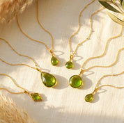 Peridot birthstone necklaces in yellow gold vermeil displayed on cream fabric in warm natural sunlight.