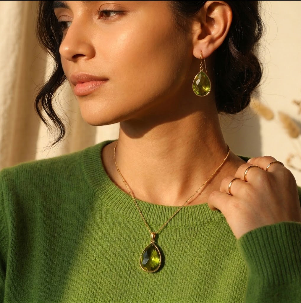 Model wearing a peridot teardrop necklace with a green sweater for an August birthstone jewelry look.
