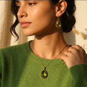 Model wearing a peridot teardrop necklace with a green sweater for an August birthstone jewelry look.
