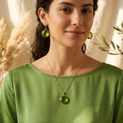 Model wearing a peridot birthstone necklace with a soft green top in natural sunlight.