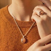 Video showcasing aSunstone necklace displayed on a warm stone surface, featuring an oval orange gemstone pendant in a gold bezel setting on a delicate gold chain.