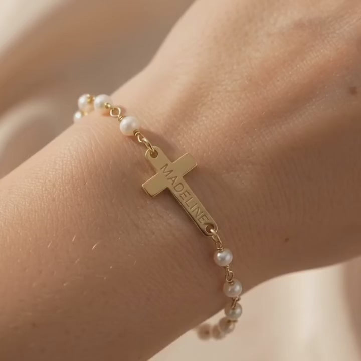 Video showcasing a dainty custom engraved cross bracelet on the wrist, featuring a slim gold bar and cross charm on a wire-wrapped natural gemstone chain; elegant personalized Christian bracelet, meaningful faith jewelry and gift for baptism, confirmation or everyday wear.